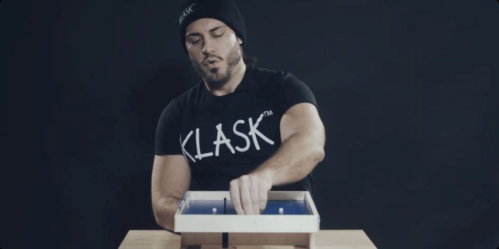 Close-up of player's hand controlling magnetic piece under Klask board demonstrating proper grip technique for accurate shooting