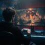 Gamer sitting in dark room facing huge glowing video game boss screen.