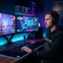 Male gamer playing on a high-performance multi-monitor desktop setup with RGB lights.