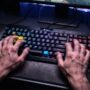 Male gamer hands typing fast on backlit mechanical gaming keyboard setup.