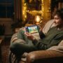 A man lying on a couch playing a cozy casual game on his phone.