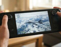 Person holding a Steam Deck playing a flight simulator game over snowy mountains.