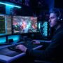 Man looking at dual gaming monitors displaying performance benchmark graphs and high-framerate gameplay.