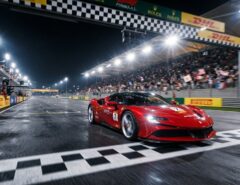 A red supercar crossing a illuminated finish line at full speed.